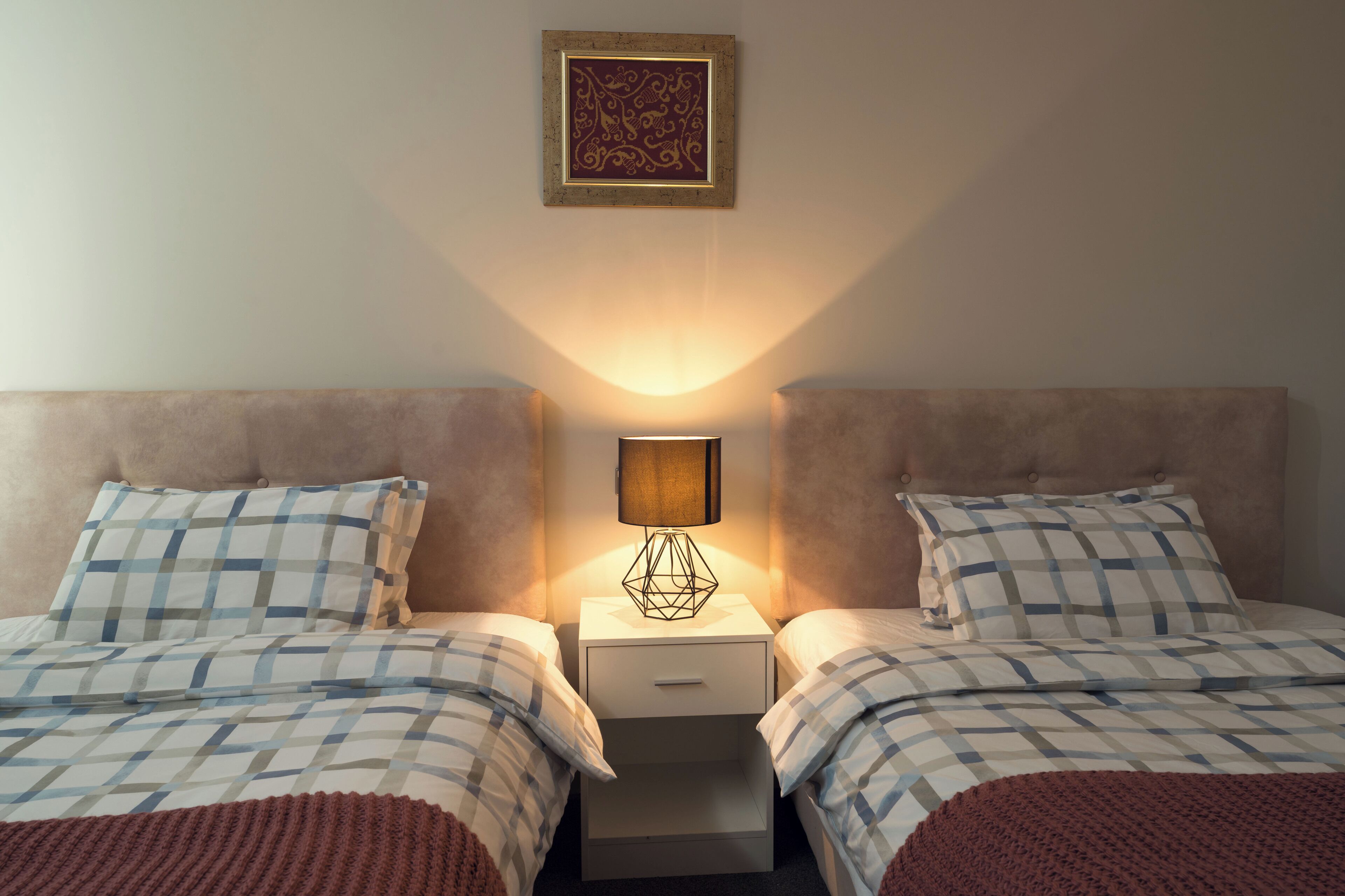 Une chambre avec deux lits, une table de chevet avec une lampe et un élément décoratif mural.