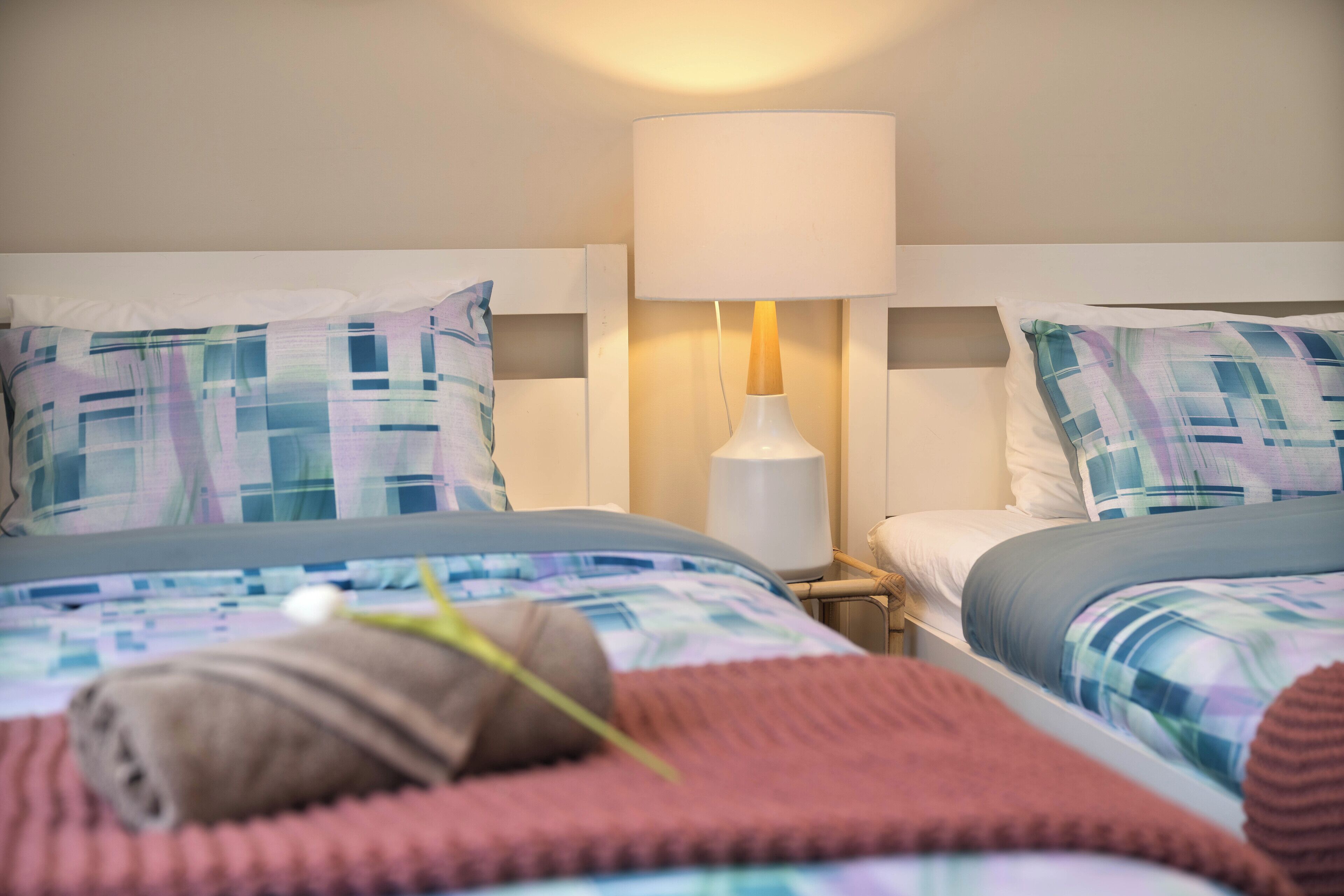 Habitación de hotel con dos camas, cada una con una colcha a cuadros y almohadas a juego. Hay una lámpara de noche en una de las camas.