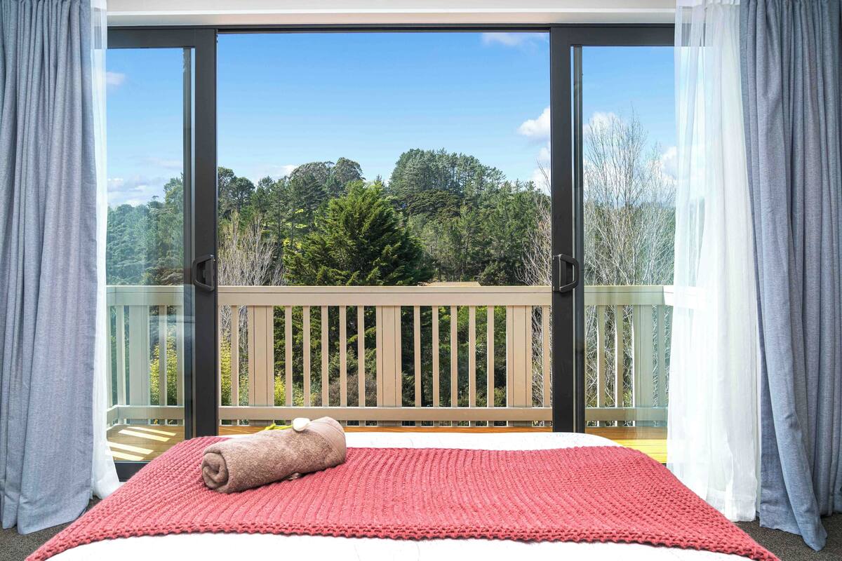 A bedroom with a large window, a red rug, and a rolled towel on the bed.