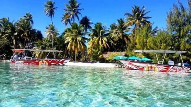 Una piscina tropical cristalina con barcos y palmeras al fondo.