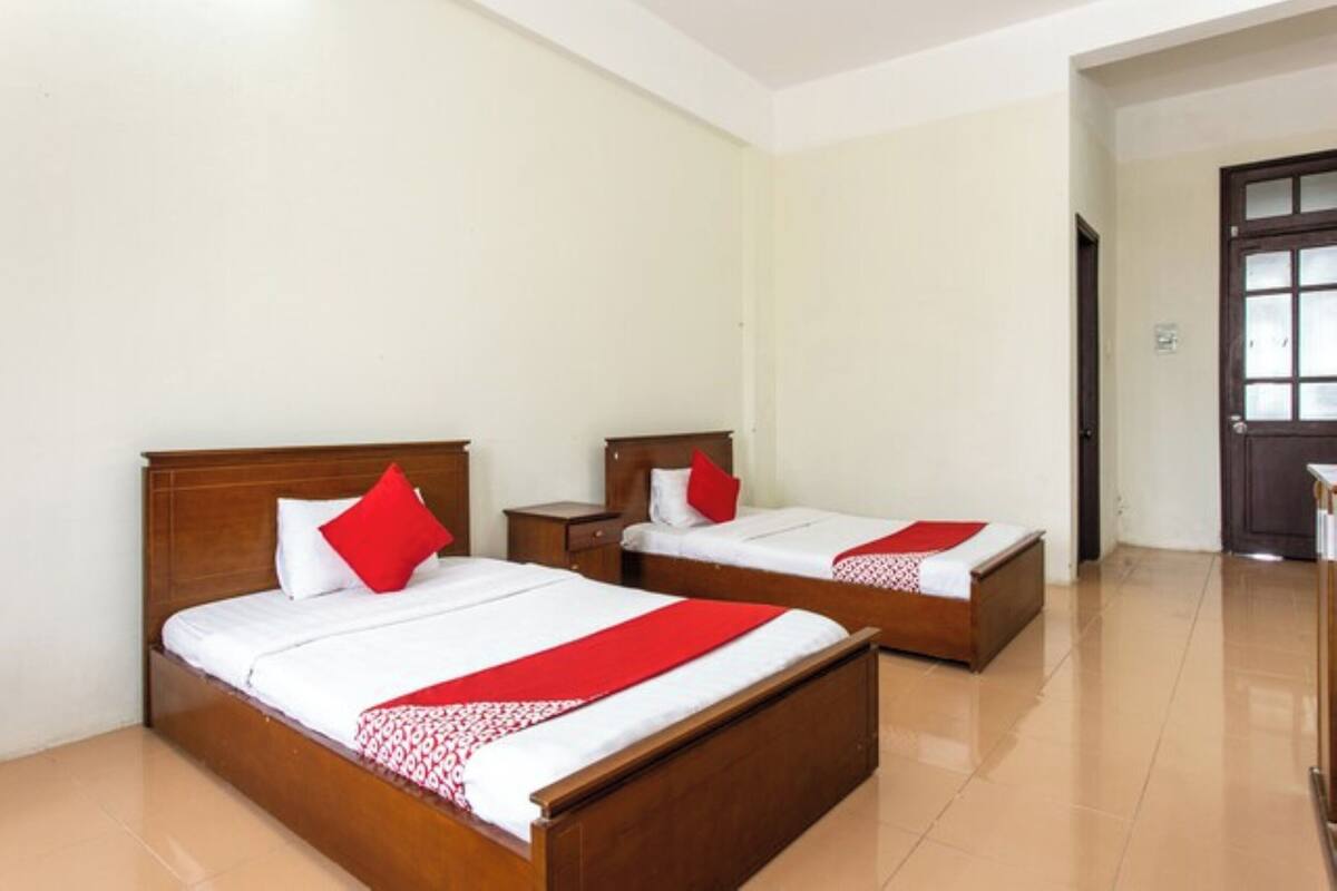 A hotel room with two wooden beds, each with a red pillow and a white bedspread.