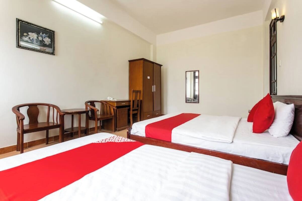 A hotel room with two beds, a desk, chairs, a wardrobe, and a mirror.