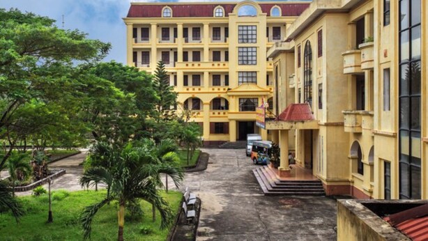 A large, yellow building with multiple windows and a red roof, surrounded by greenery and a paved courtyard. - Cua Dai Beach Hotel (Da Nang)