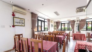 A dining area with multiple tables and chairs, air conditioning units, and large windows allowing natural light. - Cua Dai Beach Hotel (Da Nang)