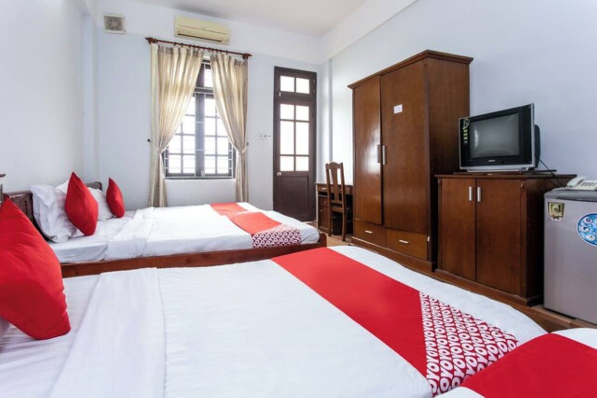 A bedroom with two beds, a wooden wardrobe, a television, and a window with curtains.