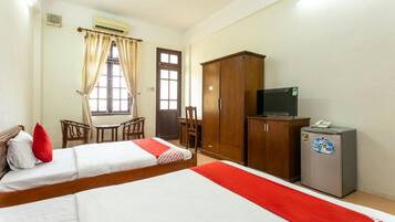A hotel room with two beds, a desk, a chair, a wardrobe, and a refrigerator.