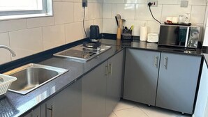 A modern kitchen with grey cabinets, a stainless steel sink, and a window providing natural light. - LivLuxe Apartments 3 (Kampala)