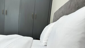 A bed with white bedding and a grey wardrobe in the background. - LivLuxe Apartments 3 (Kampala)