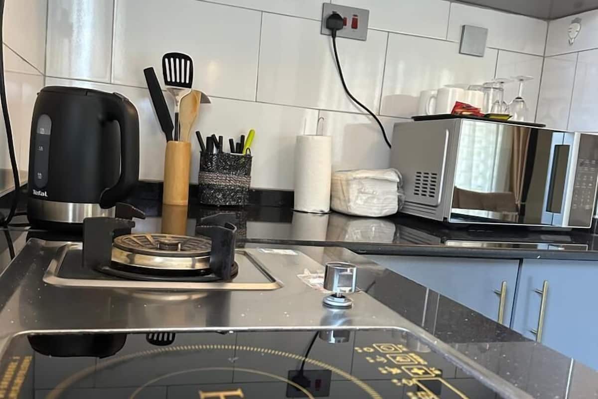 A kitchen with a black induction cooktop, a kettle, a microwave, and a coffee maker. There are utensils in a holder and a roll of paper towels on the counter.