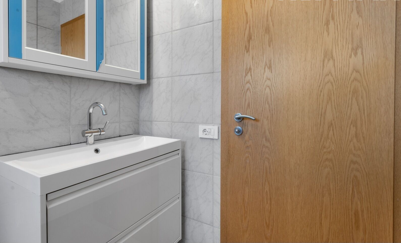 A bathroom with a white sink, a mirror, and a wooden door.