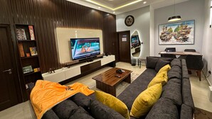 Una sala de estar moderna con un televisor de pantalla plana, un sofá con cojines amarillos, una mesa de centro y un escritorio con una computadora portátil.