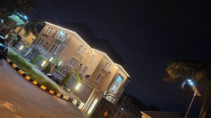Un edificio de varios pisos con una entrada porticada e iluminado por luces exteriores.