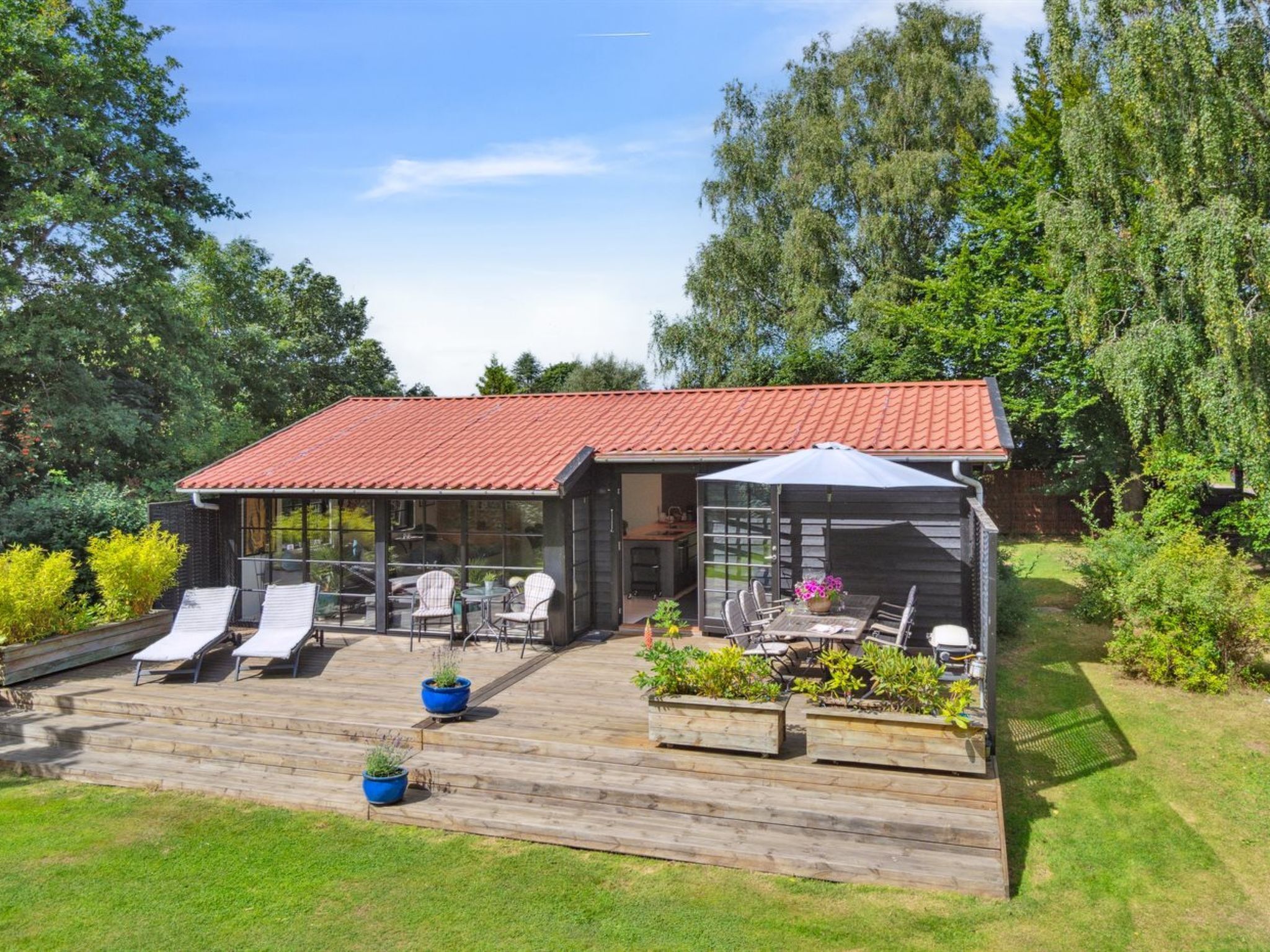 A modern house with a red-tiled roof, a covered patio with outdoor furniture, and a wooden deck.