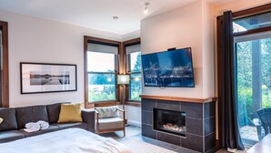 Une chambre d’hôtel moderne dotée d’un grand lit, d’un canapé, d’une cheminée, d’une télévision et de grandes fenêtres offrant une vue sur la ville.