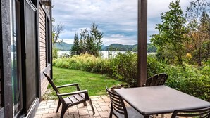 Une terrasse avec une table et des chaises, donnant sur une pelouse et un lac, avec des montagnes en arrière-plan.