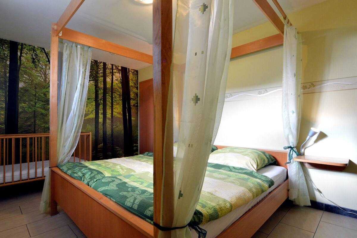 A four-poster bed with a canopy, a wooden headboard, and a green and white patterned bedspread.