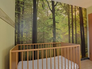 A room with a crib against a wall with a forest mural. - Comfy Holiday Home in Burg Reuland With Sauna, Terrace, BBQ (Burg-Reuland)