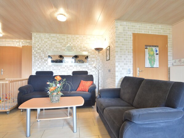 A living room with a dark blue sofa, a wooden coffee table, and a wall-mounted shelf with decorative items. - Comfy Holiday Home in Burg Reuland With Sauna, Terrace, BBQ (Burg-Reuland)