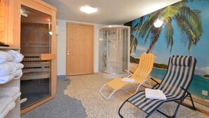 Ein Zimmer mit Sauna, einer gläsernen Dusche, zwei gestreiften Lounge-Sesseln und einem Wandgemälde mit Strandmotiv.