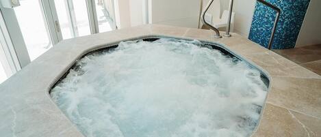 Un jacuzzi con baranda de metal, suelo de baldosas y pared de mosaico azul al fondo.