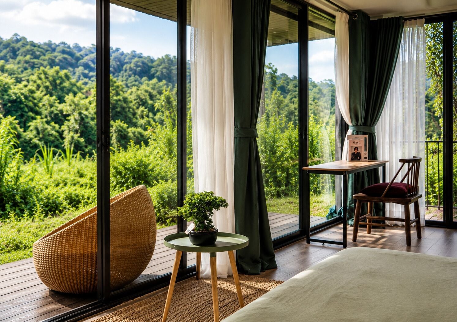 A room with a large window, a bed, a table with chairs, a wicker chair, and a small potted plant.