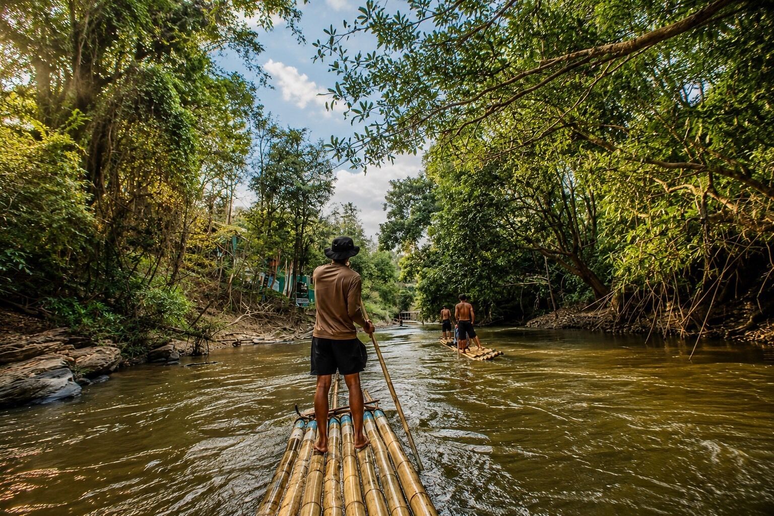 A river with people paddling on a bamboo raft.