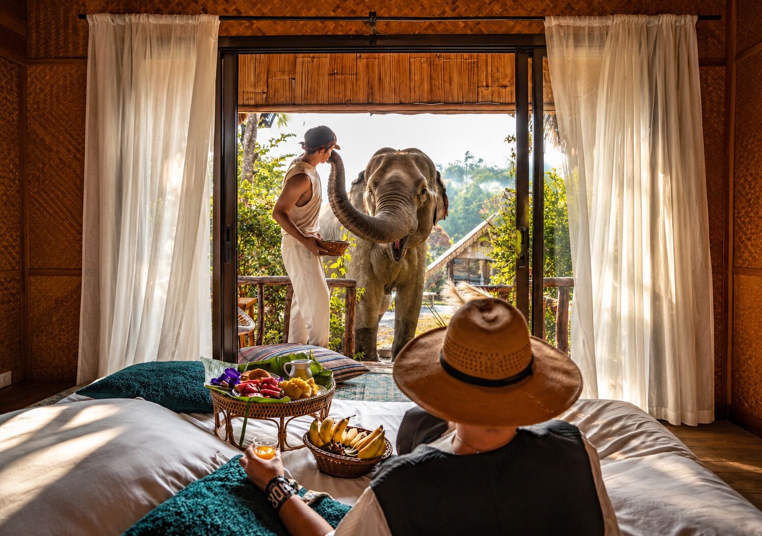 A room with a bed, a basket of fruits, and a person feeding an elephant through a window.