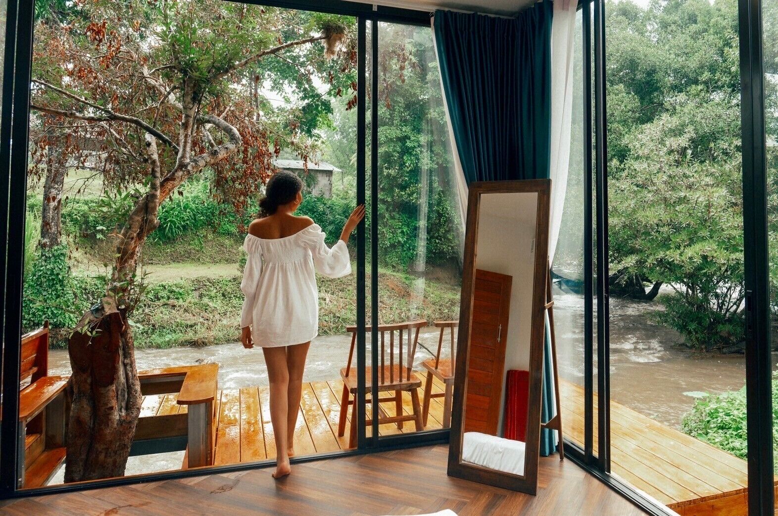 Una habitación con un amplio ventanal que da a un jardín, un banco de madera y una pequeña mesa.