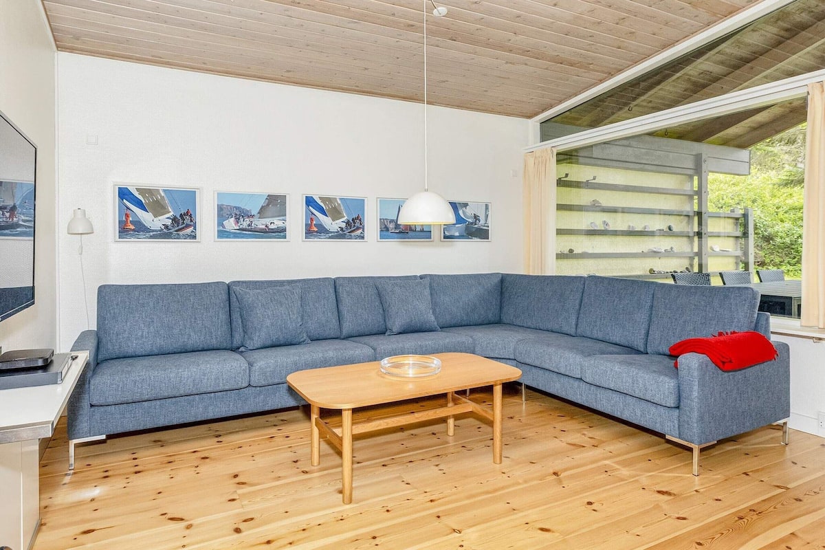 Una sala moderna con un sofá seccional azul, una mesa de centro de madera y un ventanal con vistas al exterior.