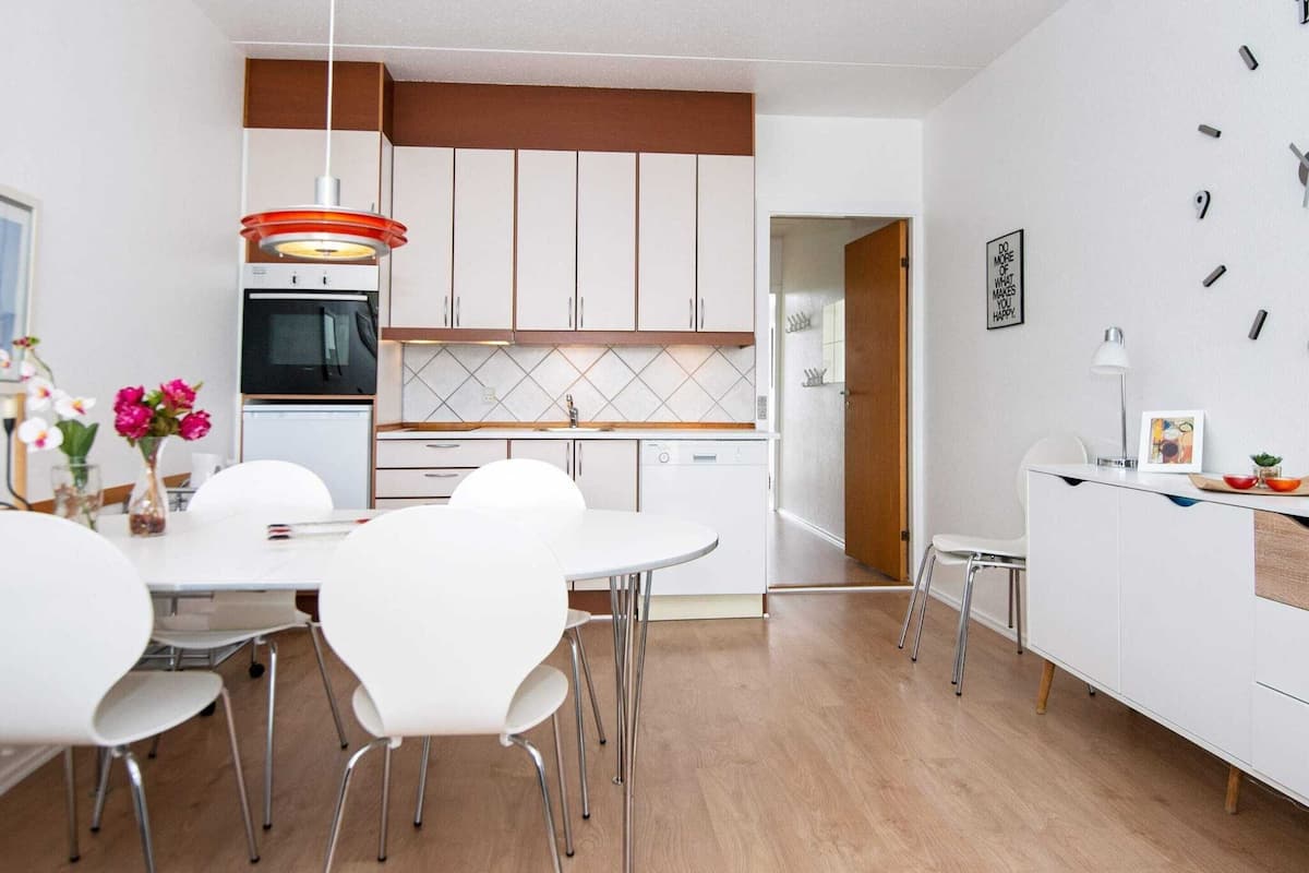 A modern kitchen with white cabinets, a wooden countertop, and a dining area with white chairs and a table.