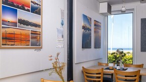 A dining area with wooden tables and chairs, a vase with dried flowers, and framed pictures on the wall.