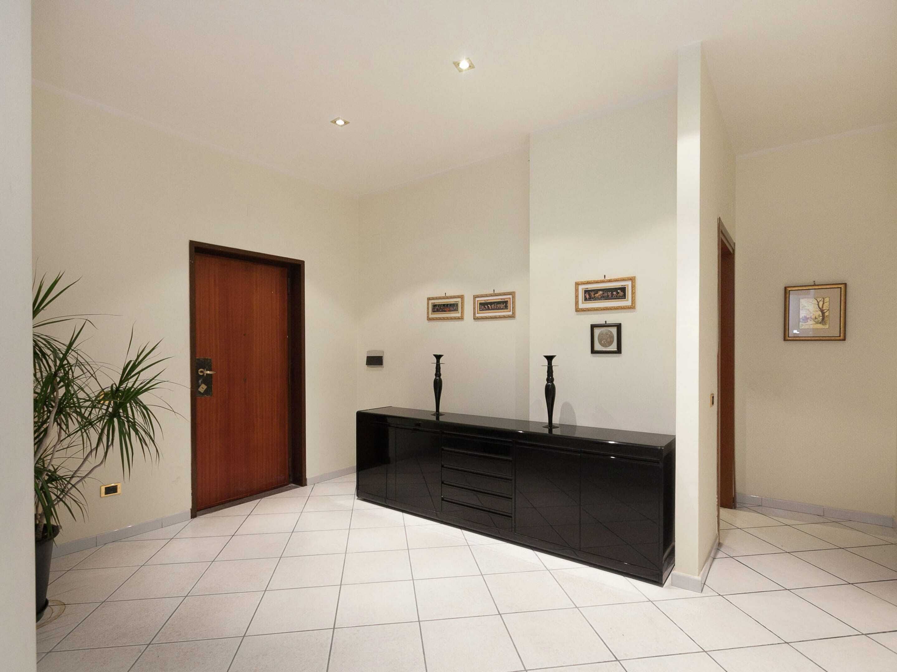 Een gang met een houten deur, een zwarte console tafel met vazen, en lijstwerken aan de wanden.