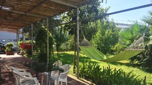 A covered patio with a table and chairs, surrounded by lush greenery and a hammock. - Apartment at the Foot of Mt. Vesuvius (Trecase)