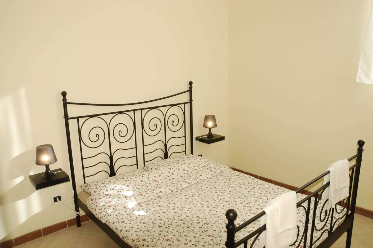 Una cama individual con una colcha estampada, dos lámparas de noche y un pequeño estante en la pared.