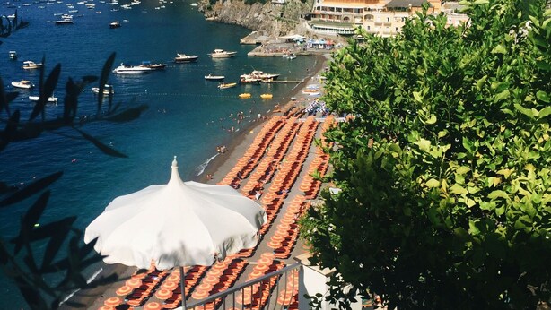 A coastal town with a beach lined with rows of orange umbrellas, boats in the water, and buildings on a hillside. - Apartment at the Foot of Mt. Vesuvius (Trecase)