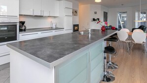 Une cuisine moderne avec des meubles blancs, un grand îlot central, des appareils en acier inoxydable et un coin repas équipé de tabourets de bar.