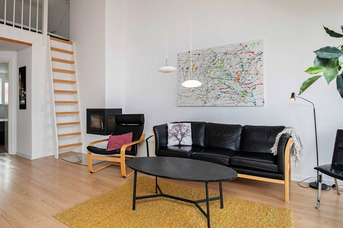 A modern living room with a black leather sofa, a wooden coffee table, a black armchair, and a colorful abstract painting on the wall.