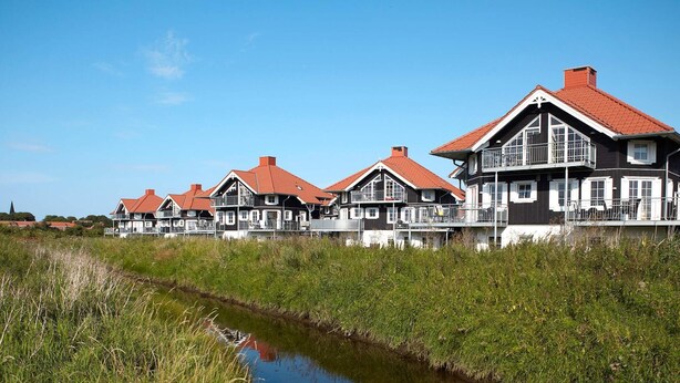 Une rangée de maisons traditionnelles aux toits rouges et aux éléments décoratifs blancs, situées au bord d’un cours d’eau paisible.