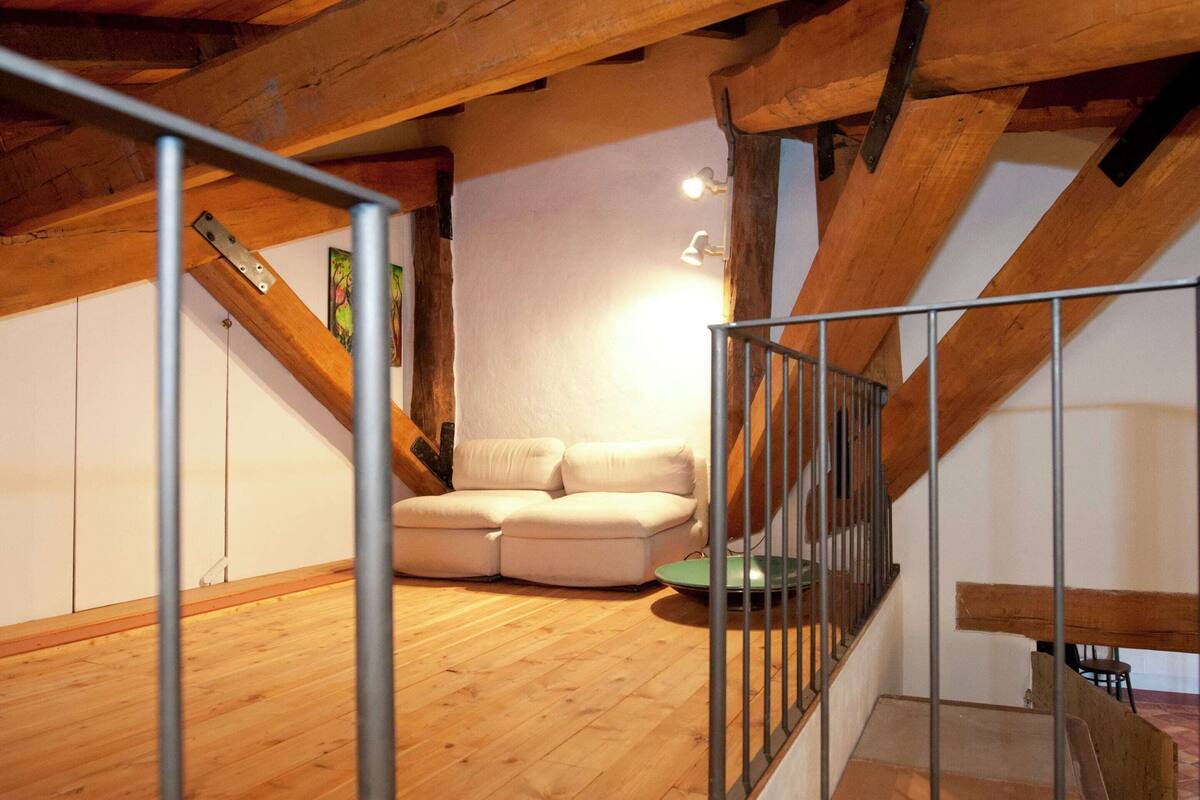 A loft-style room with exposed wooden beams, a sofa, and a staircase.