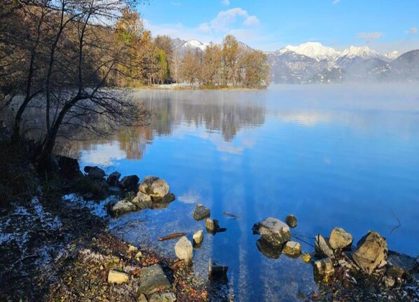 Un lago tranquilo con reflejos nítidos, rodeado de árboles y montañas al fondo.
