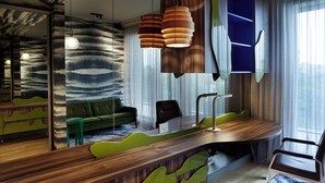 A modern interior with a curved wooden desk, a green sofa, a mirror, and a large window with sheer curtains. - Room12 (Bucharest)