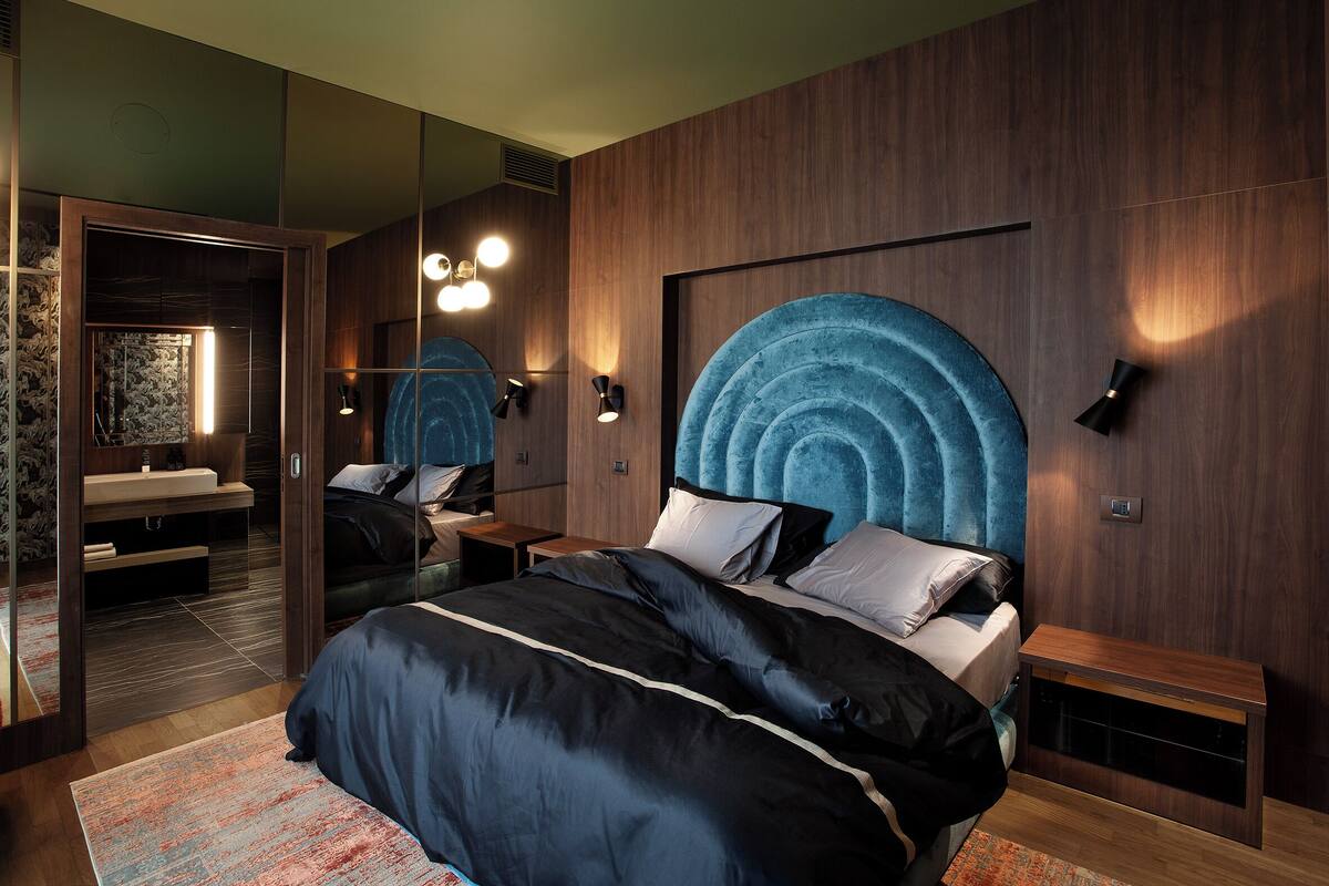 A modern bedroom with a large bed, a built-in wardrobe, a mirror, and a unique blue headboard.