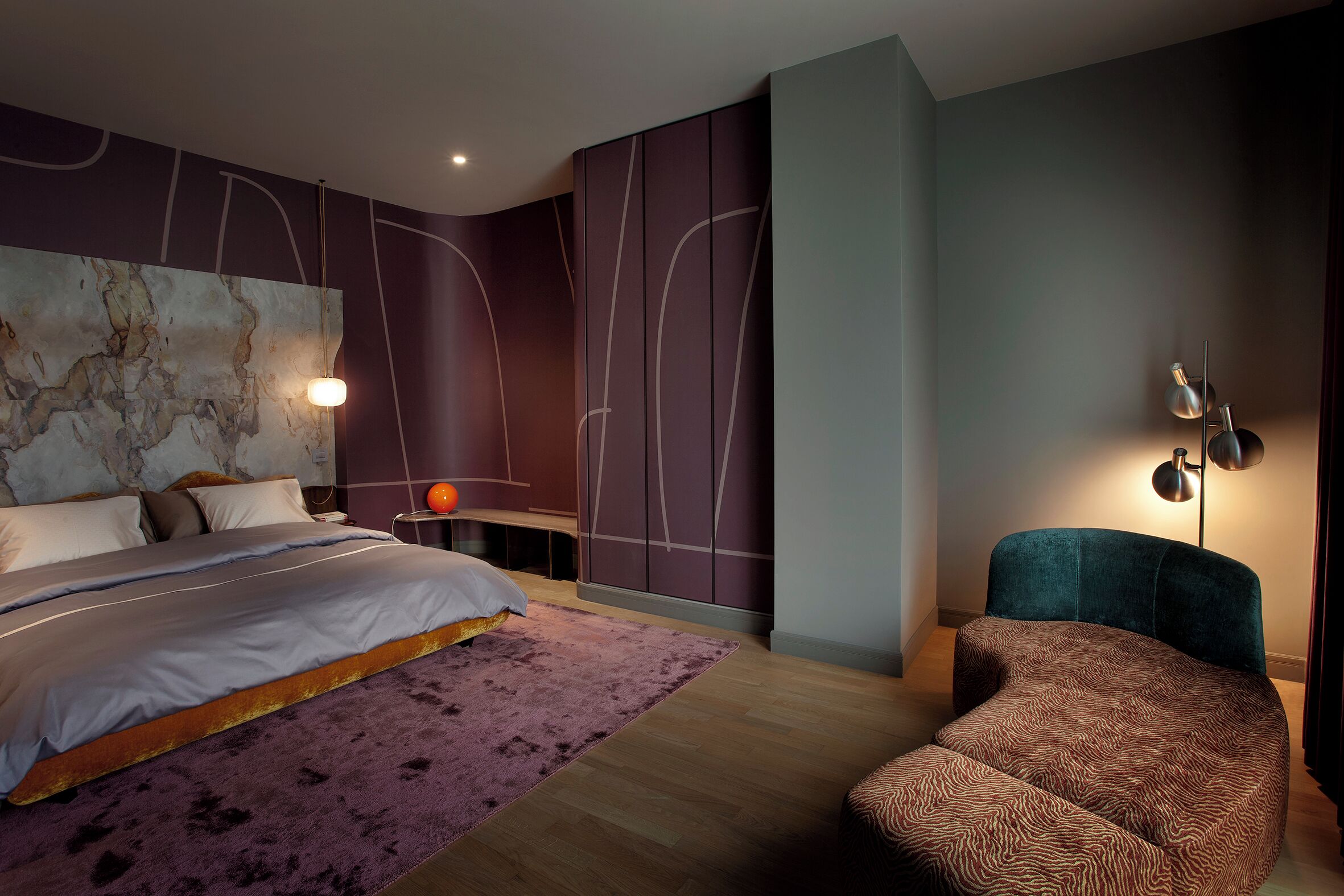 A modern bedroom with a bed, a side table, a chair, and a wall-mounted lamp.
