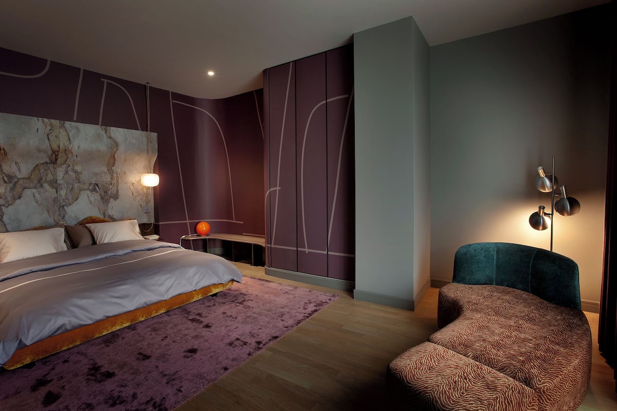 A modern bedroom with a bed, a side table, a chair, and a wall-mounted lamp.