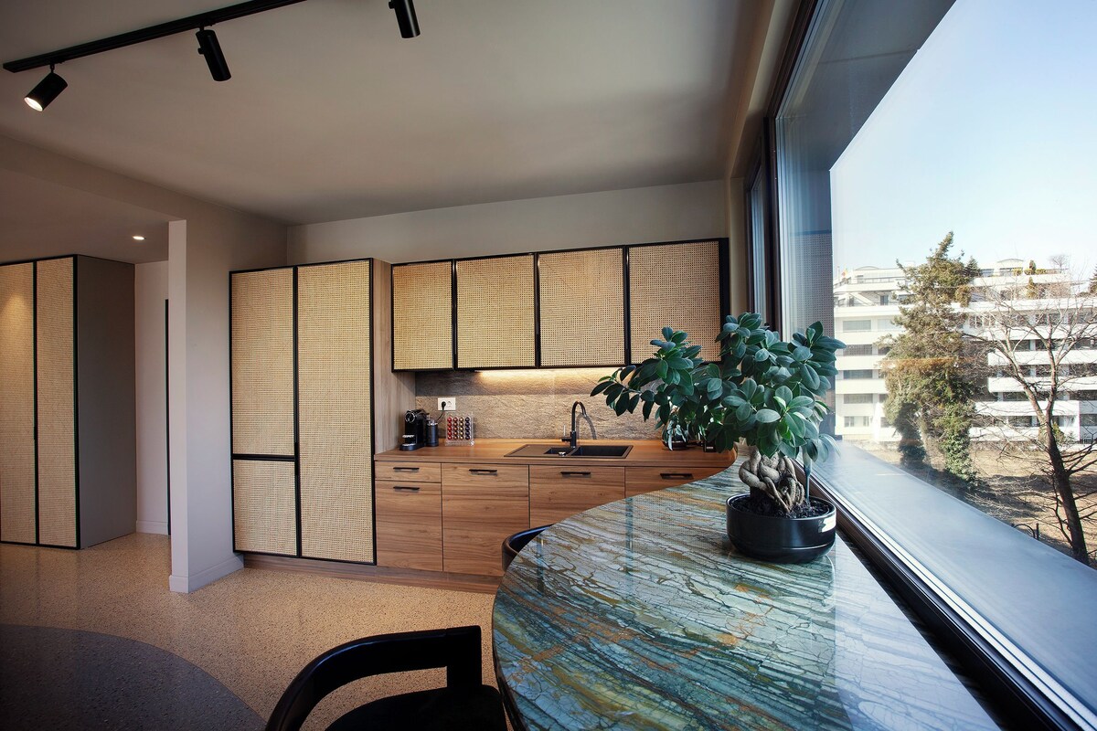 A modern kitchen with wooden cabinets, a sink, and a potted plant on a marble countertop.