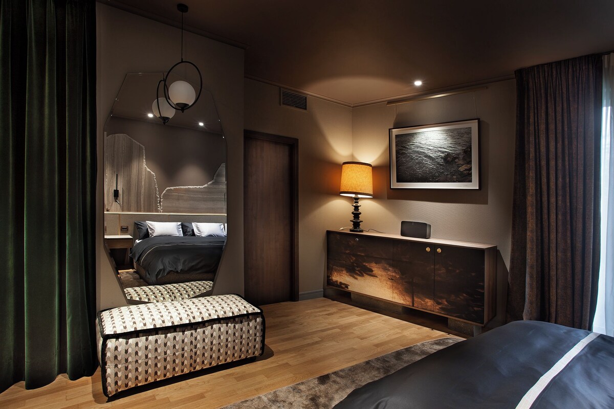 A modern bedroom with a bed, bedside table, lamp, and a painting on the wall.
