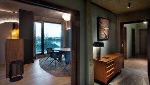 A modern hotel room with a dining area, a large window with a city view, a wooden desk, and a lamp. - Room12 (Bucharest)