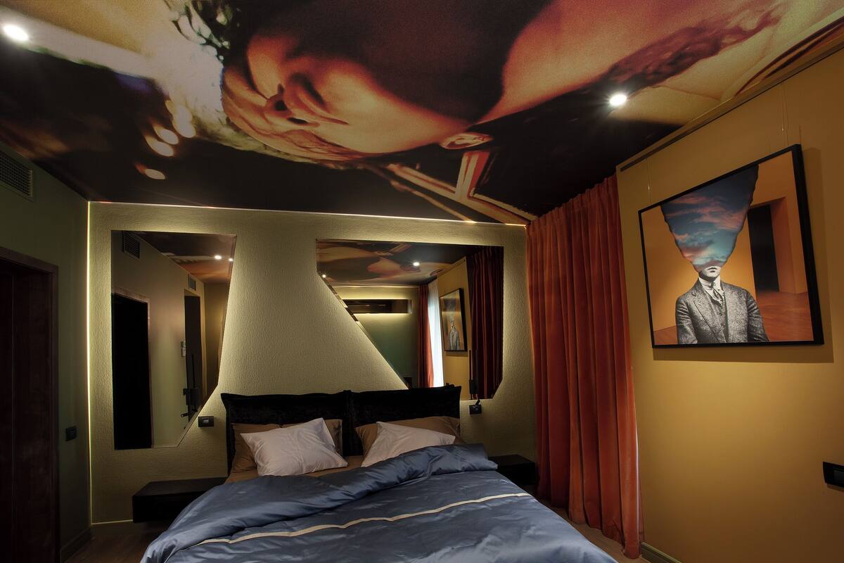 A bedroom with a bed, a ceiling mural, and a framed picture on the wall.
