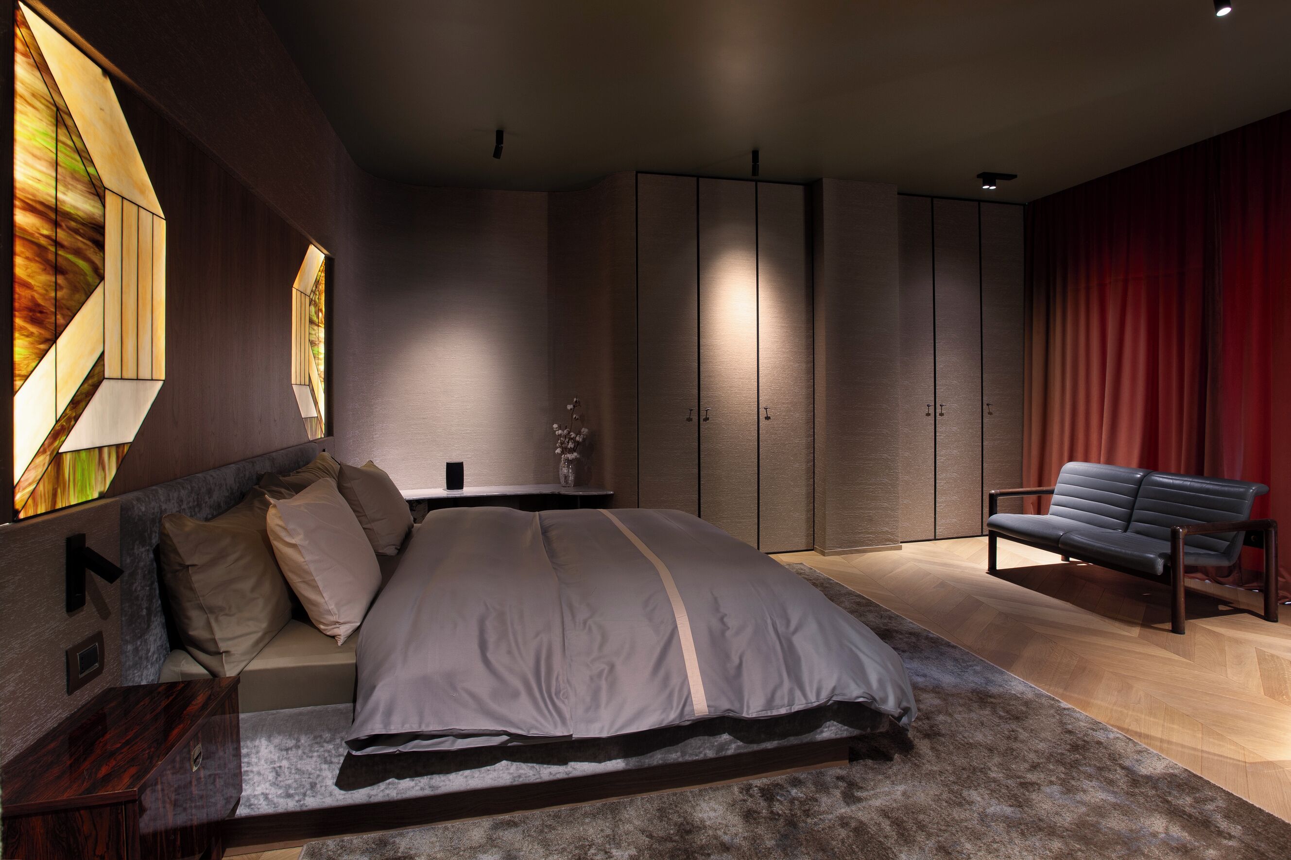 A modern bedroom with a large bed, a sofa, and built-in wardrobes.