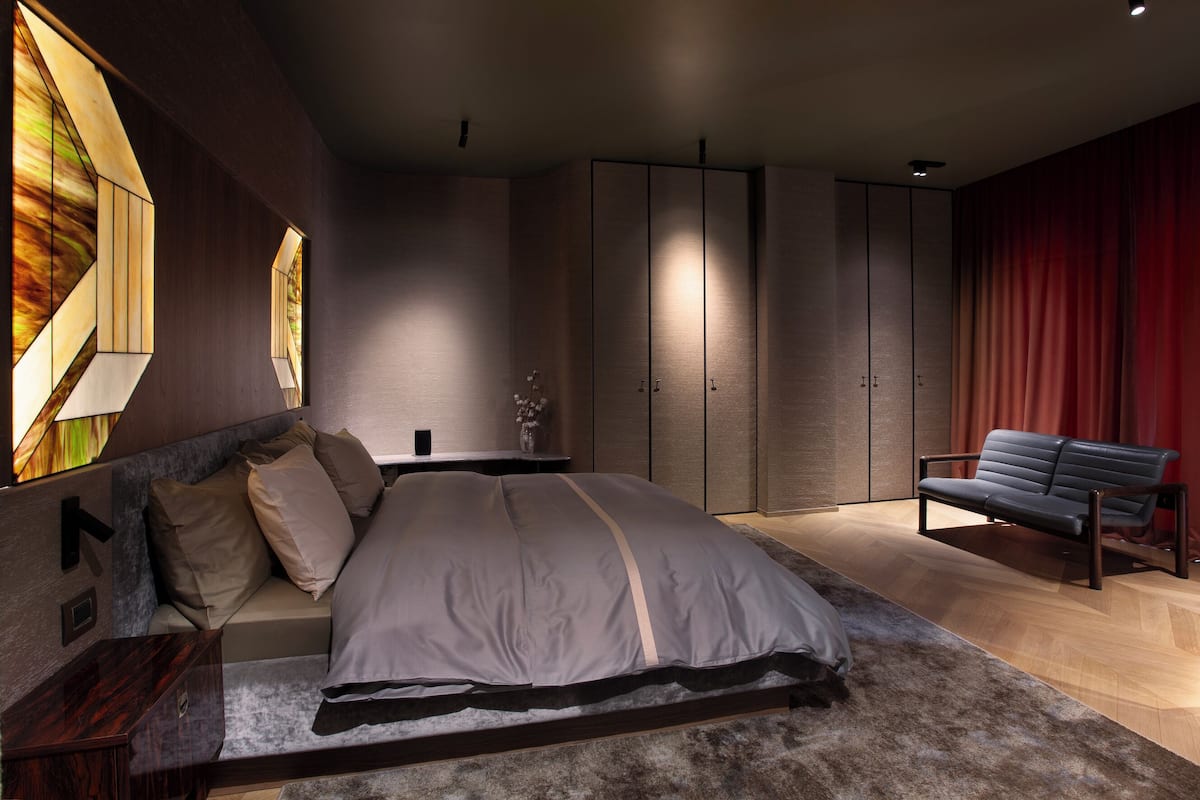 A modern bedroom with a large bed, a sofa, and built-in wardrobes.